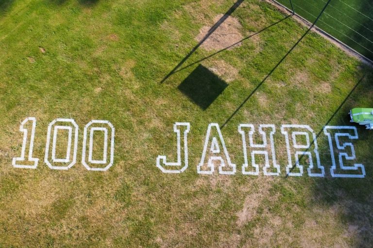 Logo-Markierung ‚100 Jahre‘ auf Sportplatz mit Markierungsroboter aus der Luft aufgenommen